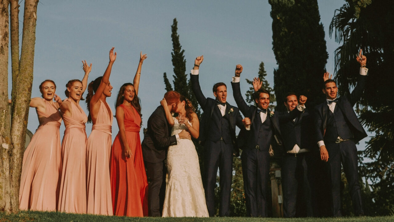 La coppia insieme alle damigelle e i tesmoni dello sposo mentre festeggiano tutti insieme, alzando le braccia al cielo mentre la coppia si bacia